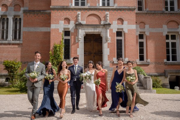 Bride groom bridesmaids and groomsmen walk in the sunshine together